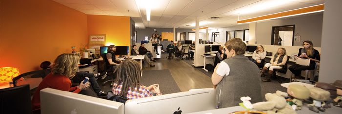 Fun group of folks sitting around at a digital marketing agency, gabbing and pinging check-ins as they touch base.